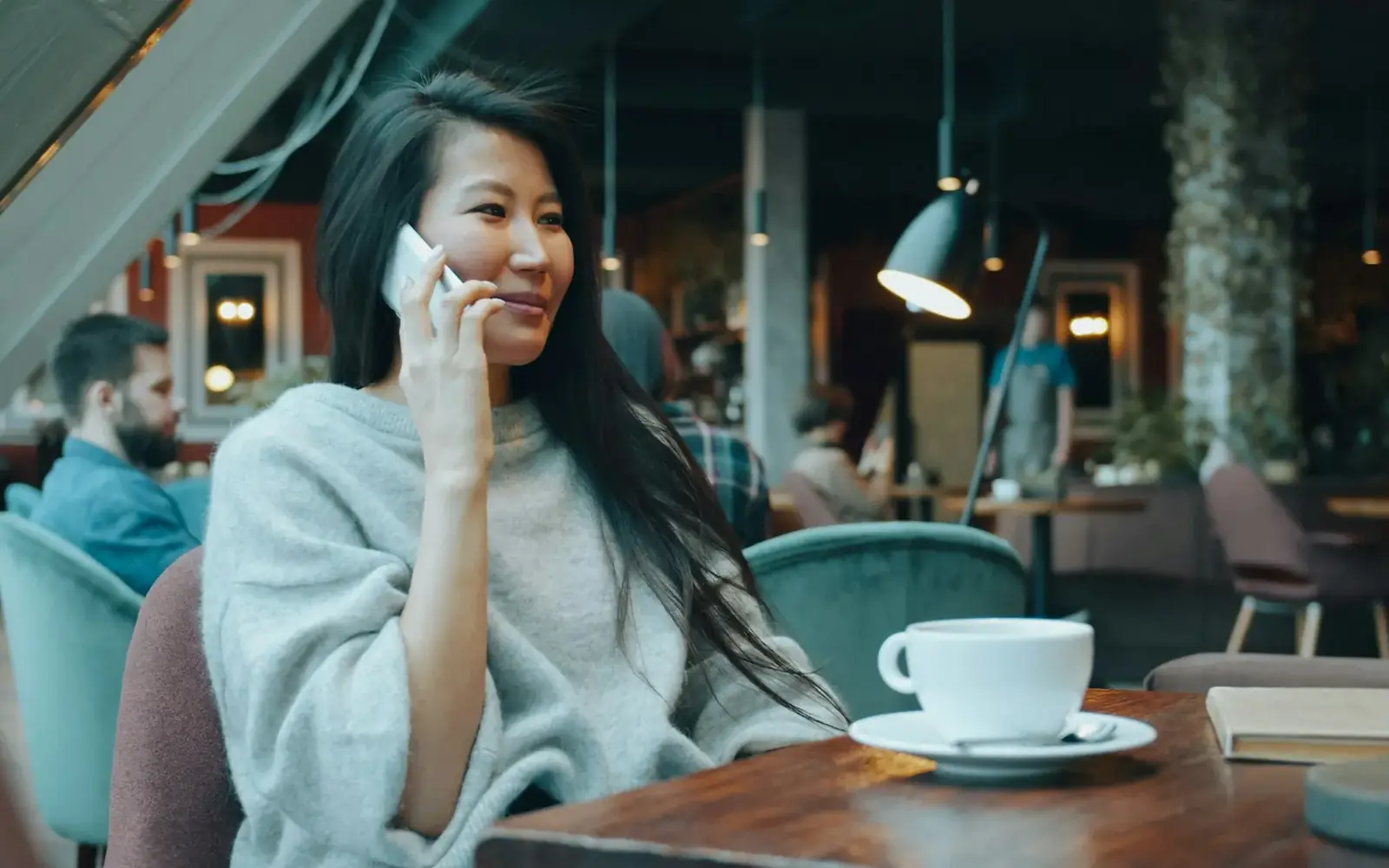 Žena u kafiću razgovara na mobitel i smiješi se